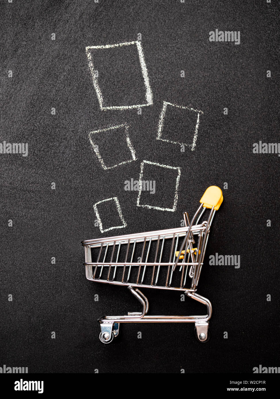 Shopping cart and products on chalkboard. Shop trolley at supermarket as sale, discount, shopaholism concept. Top view or flat lay. Vertical Stock Photo