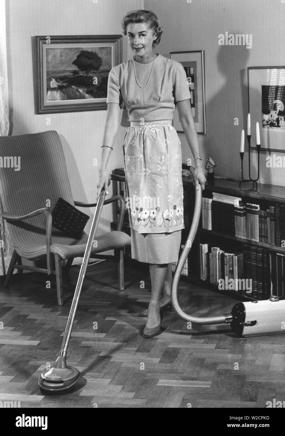 Cleaning day in the 1950s. A young housewife is vacuuming the floor using the latest model from Electrolux. The model can also be used to polish floors and she uses the device. Sweden 1950 Stock Photo