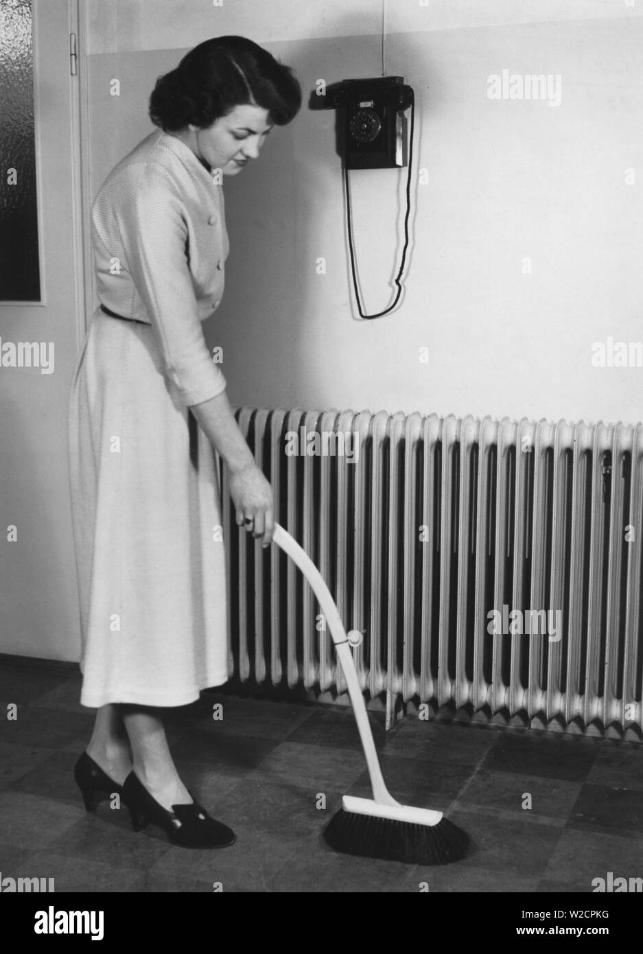 Cleaning day in the 1940s. A young woman is cleaning her apartment and is using a bush with an telescoping handle. A new invention to stand up straight when dusting and avoid back pains. Sweden 1949 Stock Photo