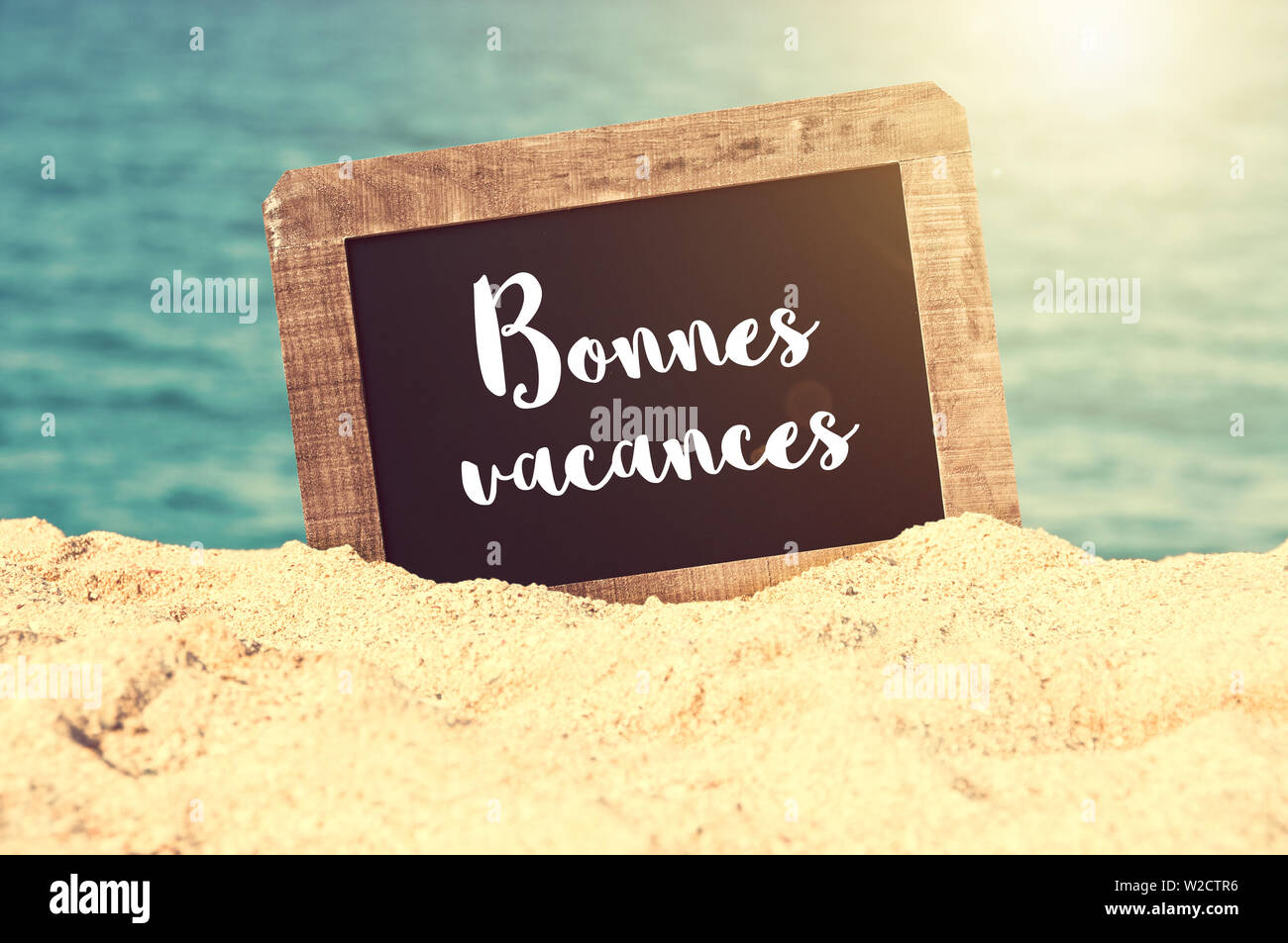 Bonnes vacances (meaning Happy holiday in French) written on a vintage chalkboard in the sand of a beach Stock Photo