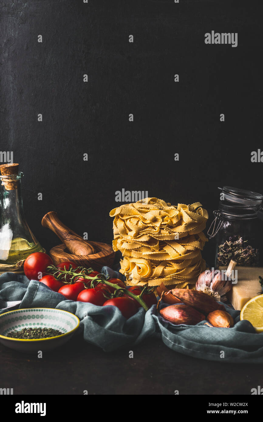 Homemade italian pasta with cooking ingredients on dark rustic kitchen table at wall background. Copy space. Italian cuisine. Still life Stock Photo