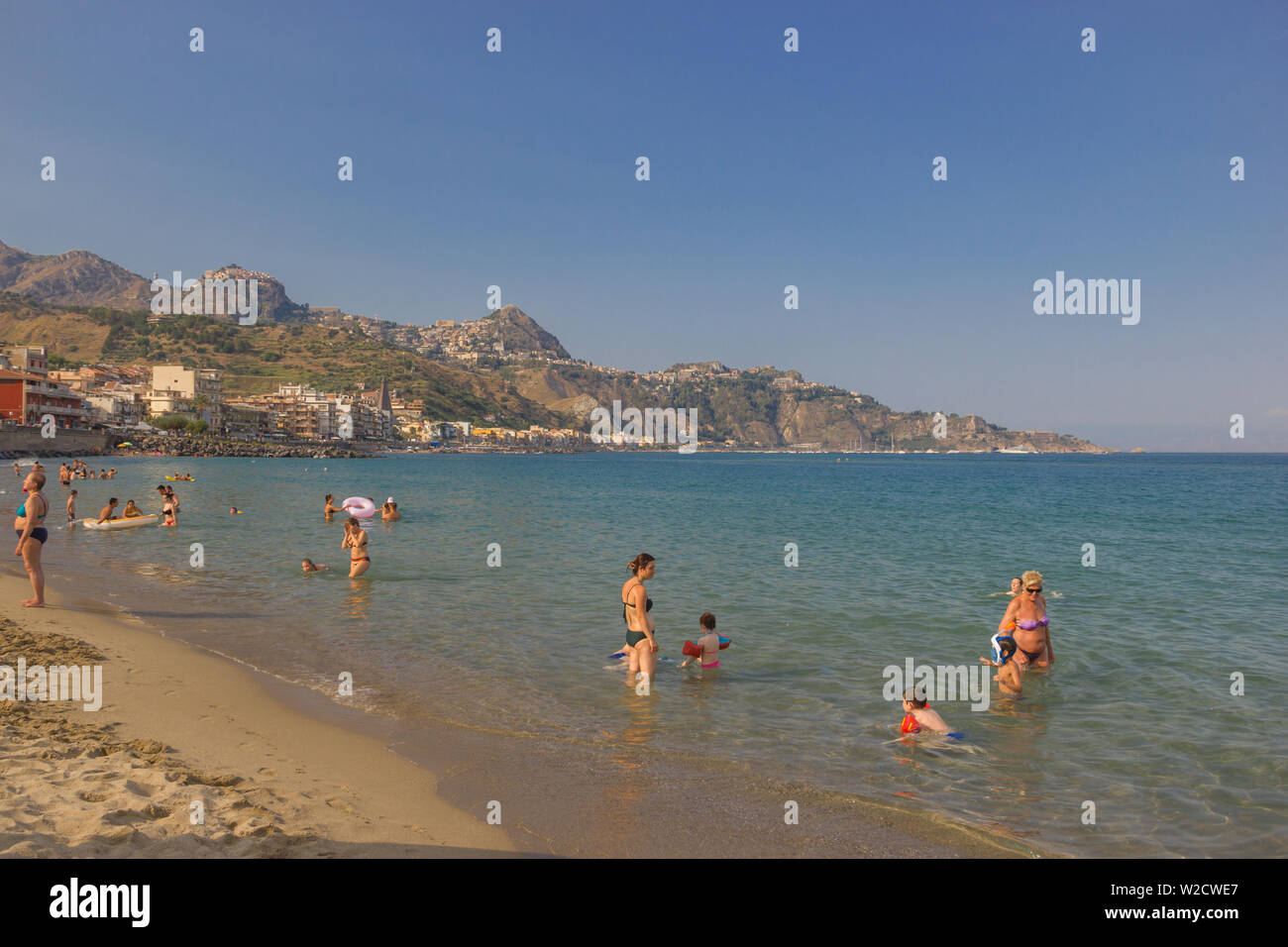 Giardini Naxos Sicily Italy 2019 Summer vacation picture with people enjoying the beach and beautiful sea, with coastline and far Taormina Stock Photo