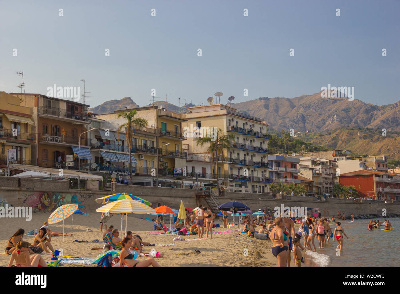 Giardini Naxos Sicily Italy 2019 view of the popular beach crowded of tourists and people, the buildings along the street facing the sea Stock Photo