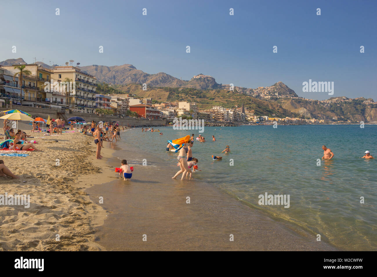 Giardini Naxos Sicily Italy 2019 Summer holiday beach with people playing and enjoying the sea, coastline and mountains Stock Photo