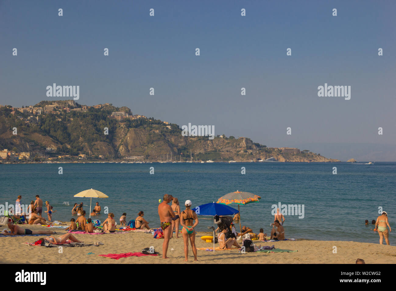 Giardini Naxos Sicily Italy 2019 beautiful view of the beach and people enjoying the sea and far in background the mountains of Taormina and bay Stock Photo