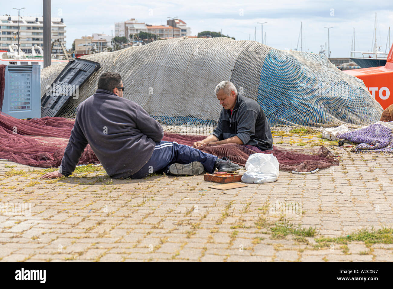 Fisherman Repairing fishing nets on the quayside at Palamos with interested onlooker Stock Photo