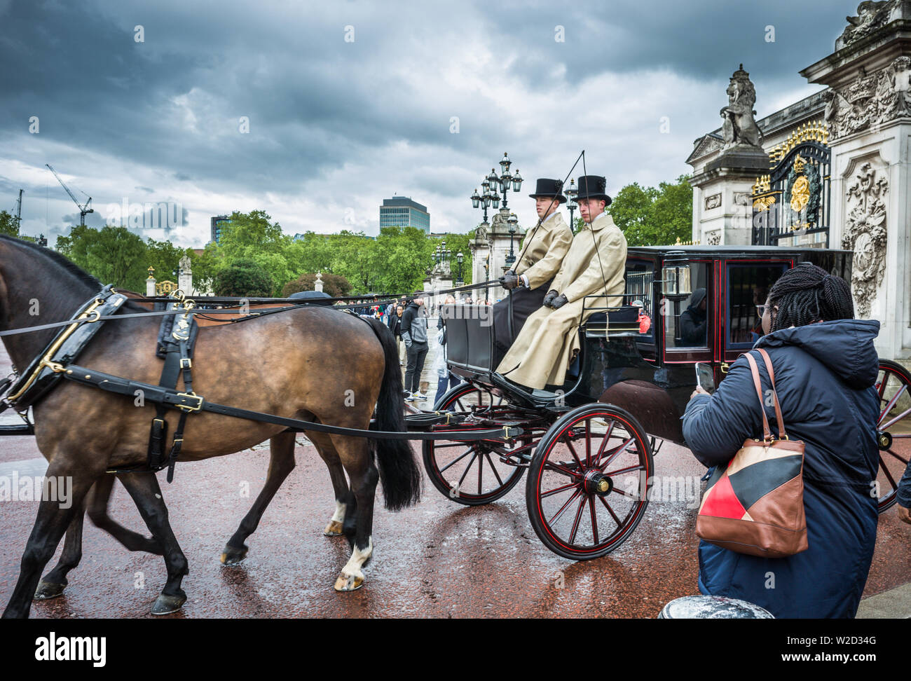 London: 9th May, 2019 Horse and carriage passes out of the gates gates Buckingham Palace as a tourist takes a photograph on her phone. Stock Photo