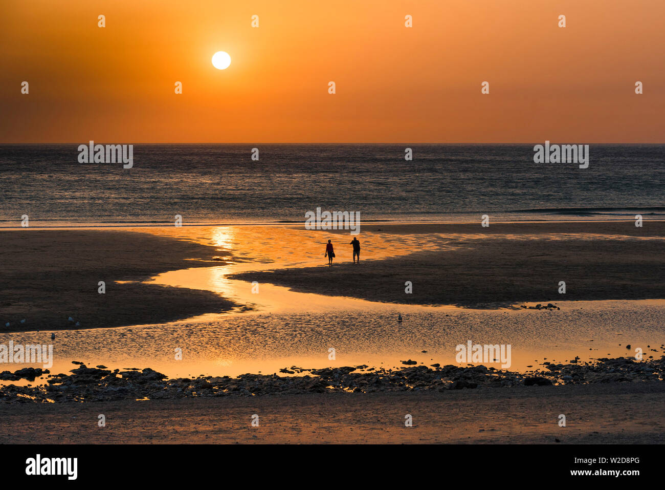 People seen in silhouette as a beautiful sunset sets over Fistral Beach in Newquay in Cornwall. Stock Photo