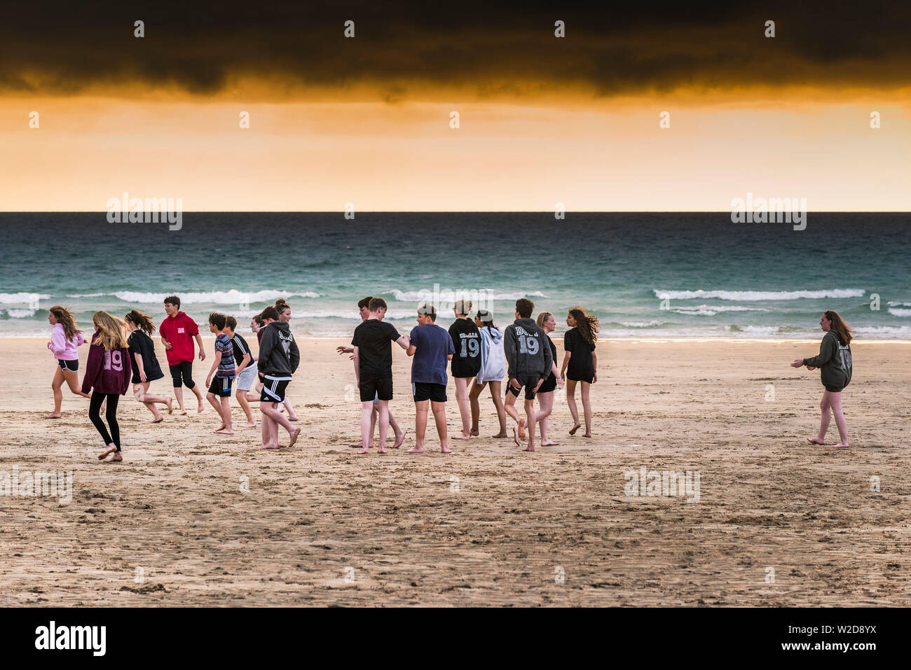 A group of teenagers hanging out on Fistral Beach during a dramatic sunset in Newquay in Cornwall. Stock Photo