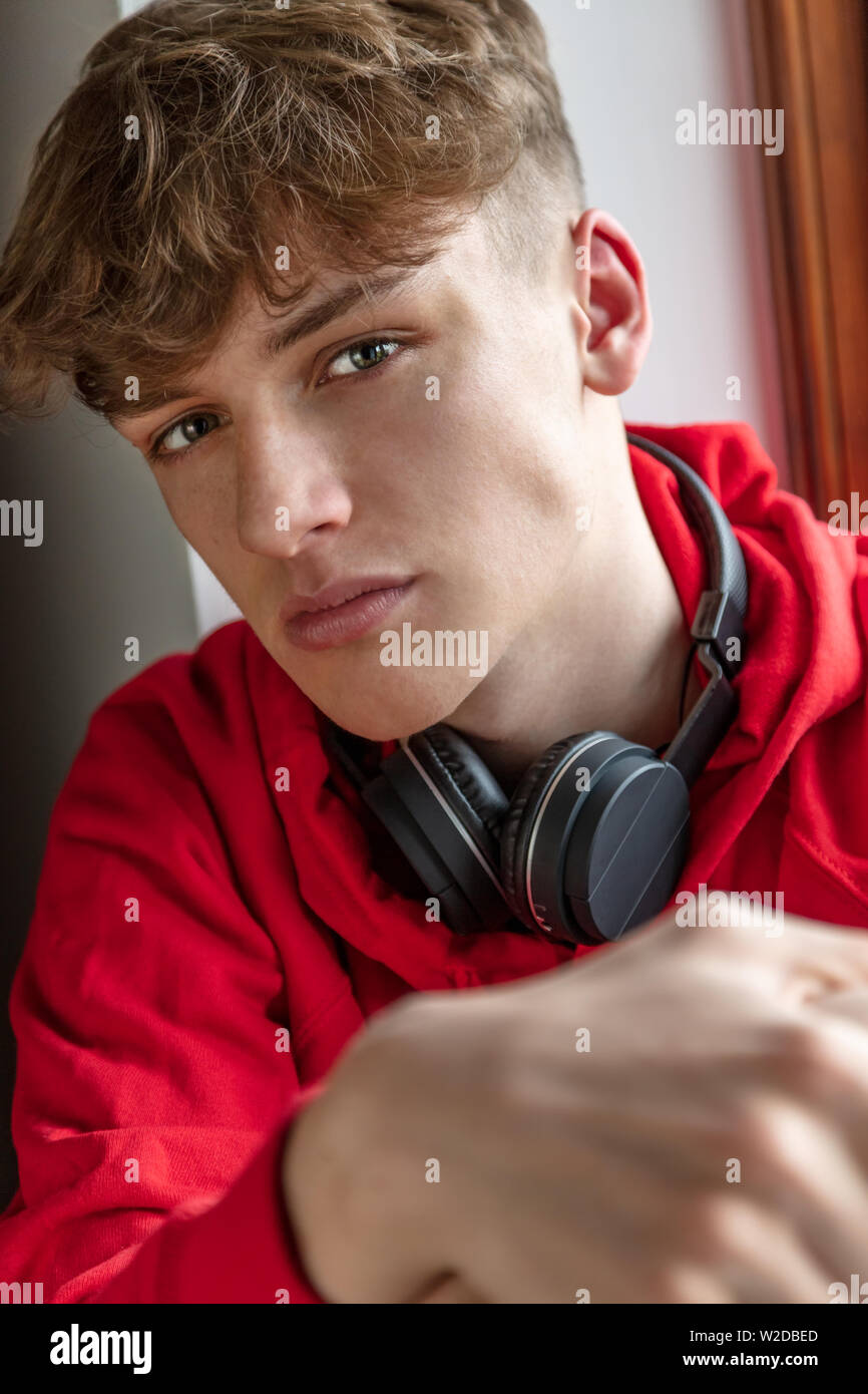 Serious moody male boy teenager young adult man indoors wearing a red hoodie and black wireless bluetooth headphones Stock Photo