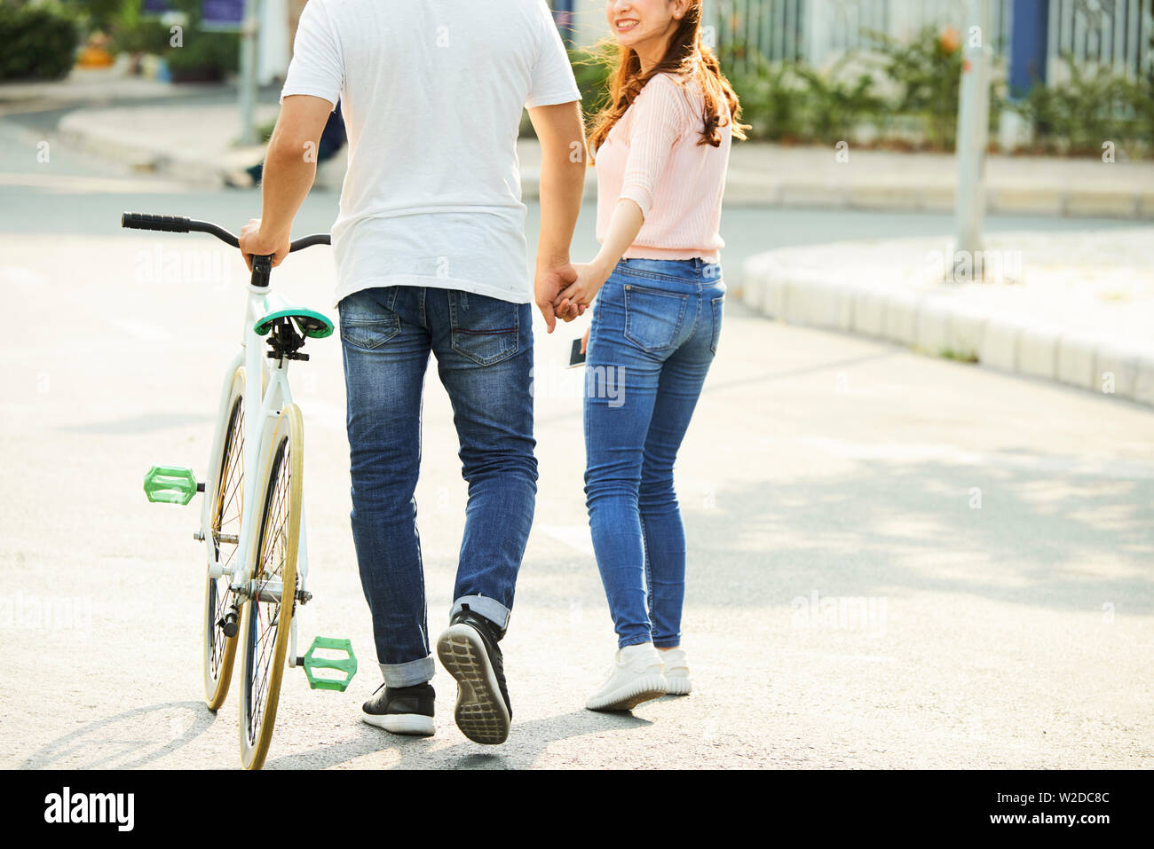 Rear view of young Asian couple with bicycle walking along the street together and holding hands Stock Photo