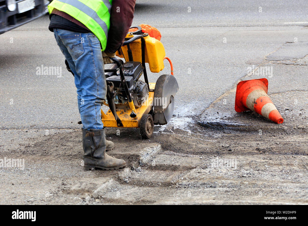 An employee of the road maintenance service removes old asphalt with a gasoline carver during repairs on the carriageway. Stock Photo