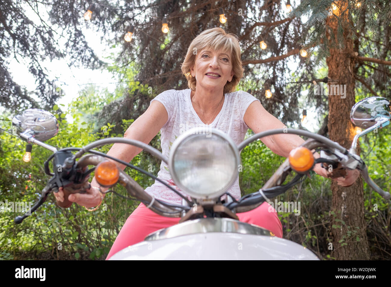 Cheerful senior woman riding a vintage scooter outdoor Stock Photo