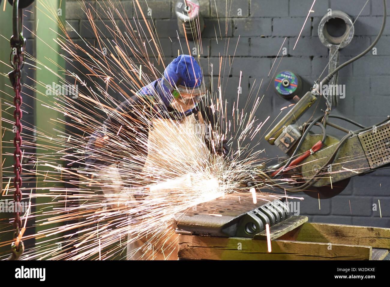 Workers in protective equipment in a foundry work on a casting with a grinding machine at the workplace Stock Photo