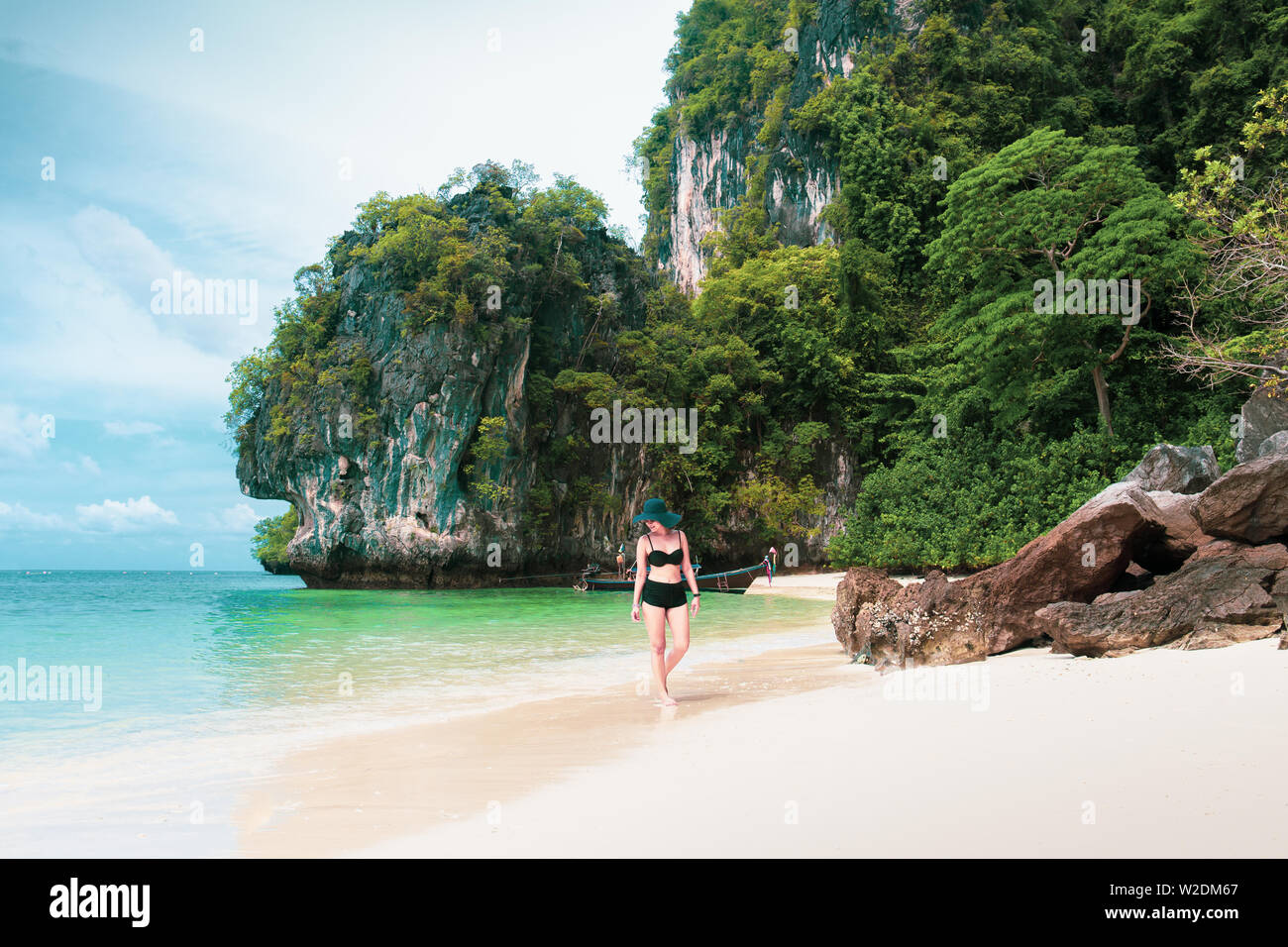 Happy smiling woman in bikini and sunhat walking on sea beach. Stock Photo
