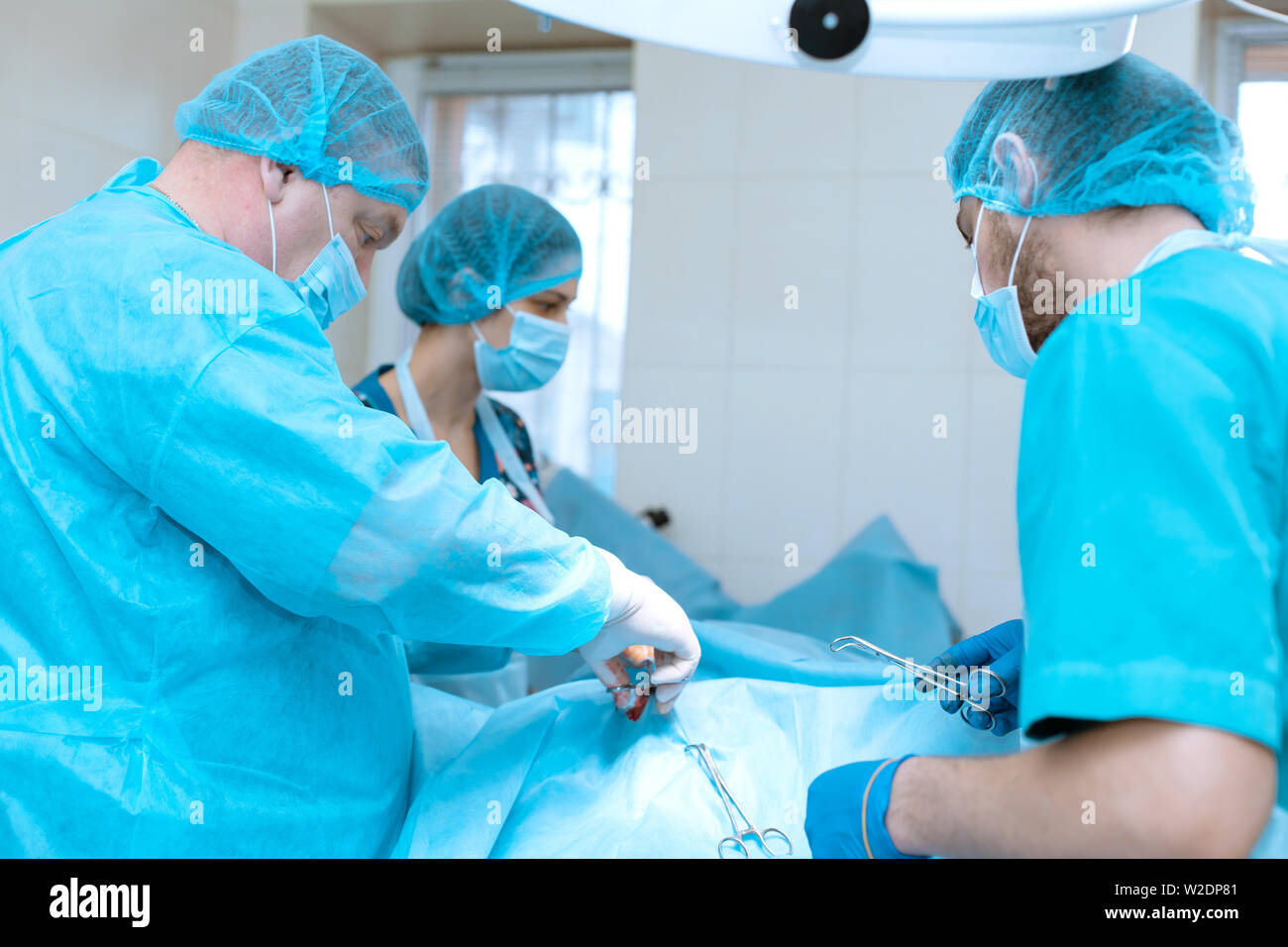 An Experienced Surgeon In A Mask And Gown Operates In A Sterile Operating Room With An Assistant 