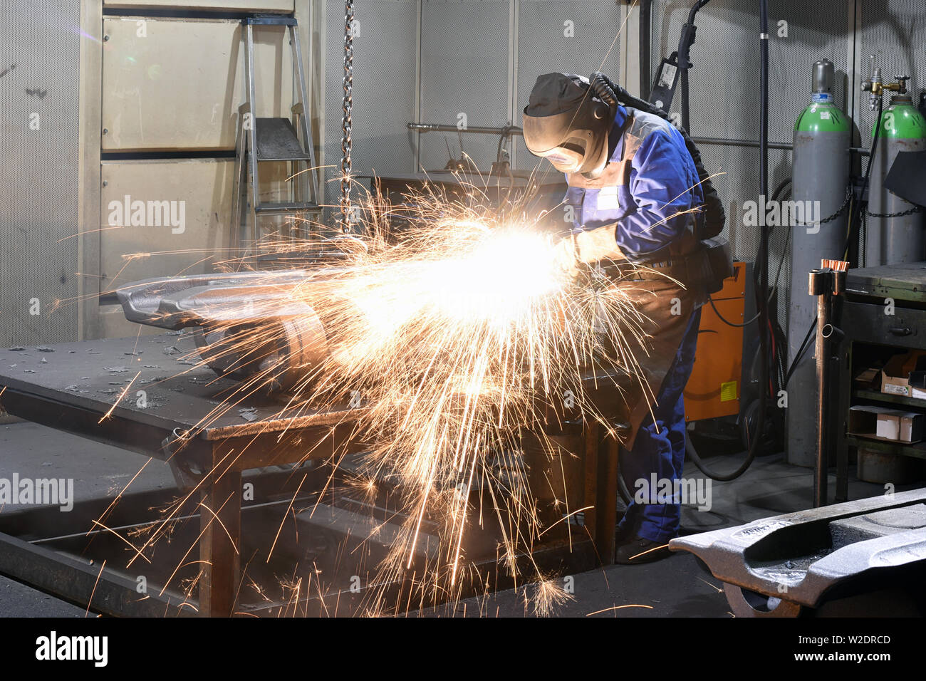 Workers in protective equipment in a foundry work on a casting with a grinding machine at the workplace Stock Photo