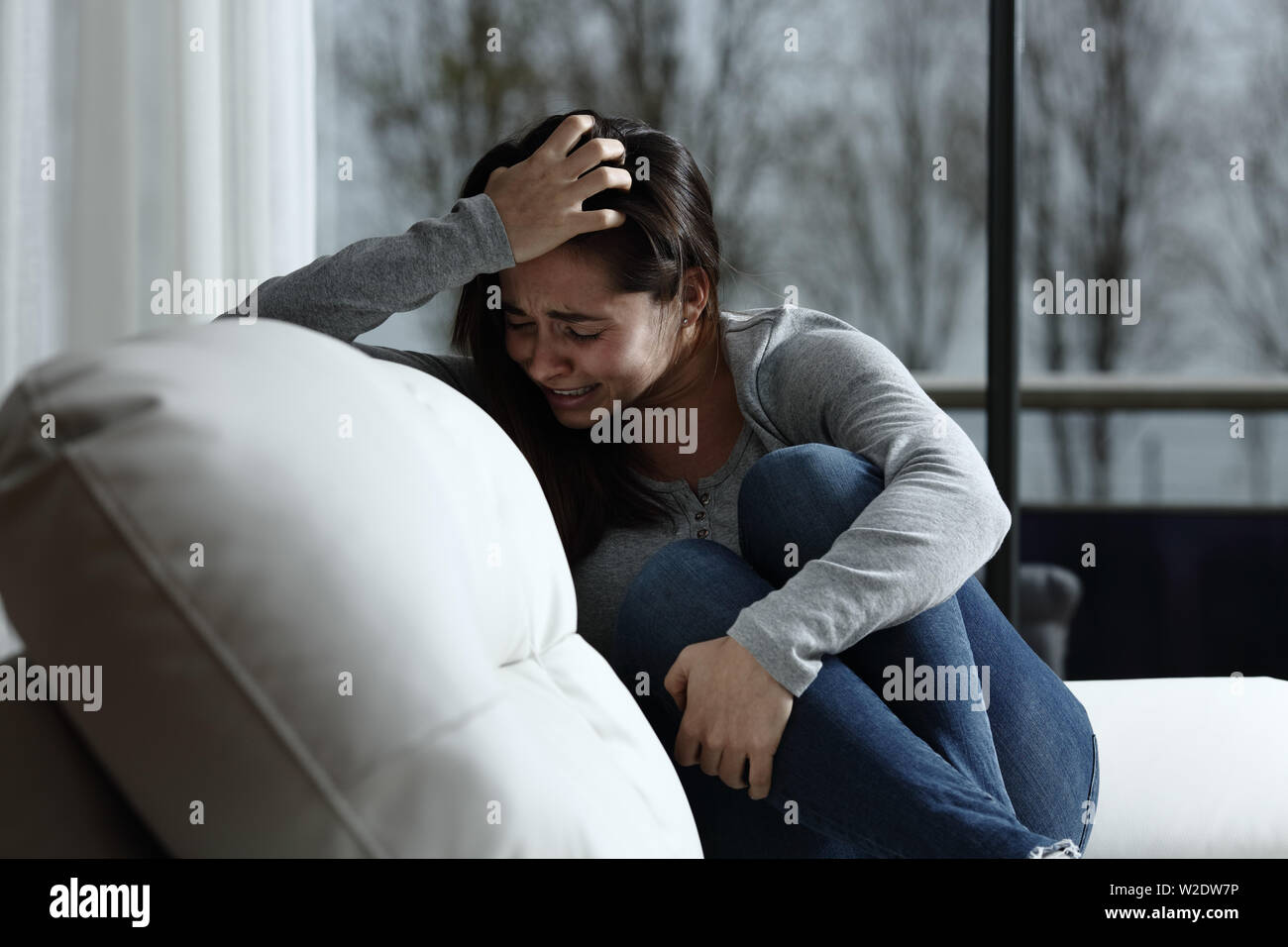 Sad woman complaining and crying sitting on a couch in the living room at home Stock Photo
