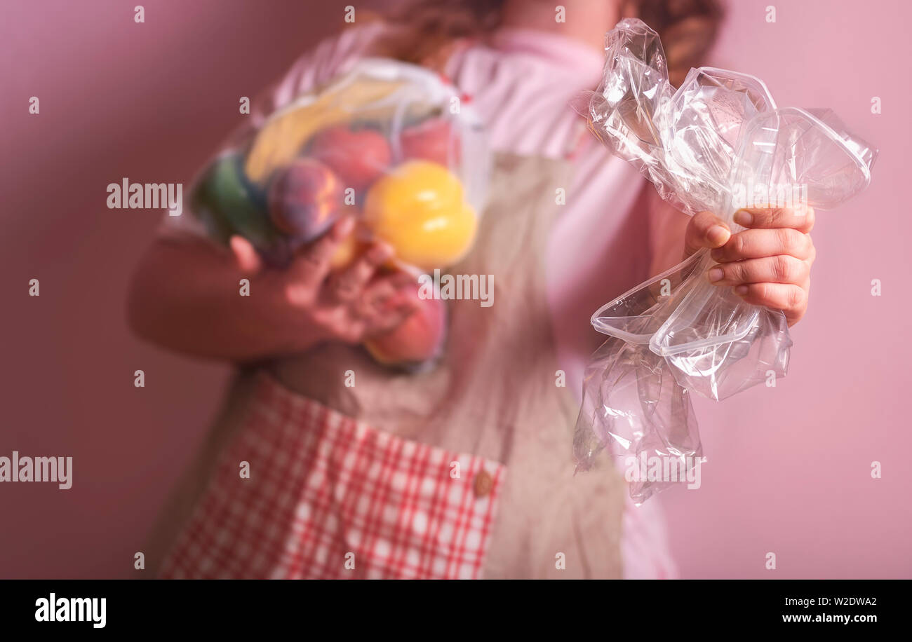 Woman squeezing empty plastic wrappers in one hand and holding the groceries in an eco-friendly reusable bag. Waste reduction at home concept. Stock Photo