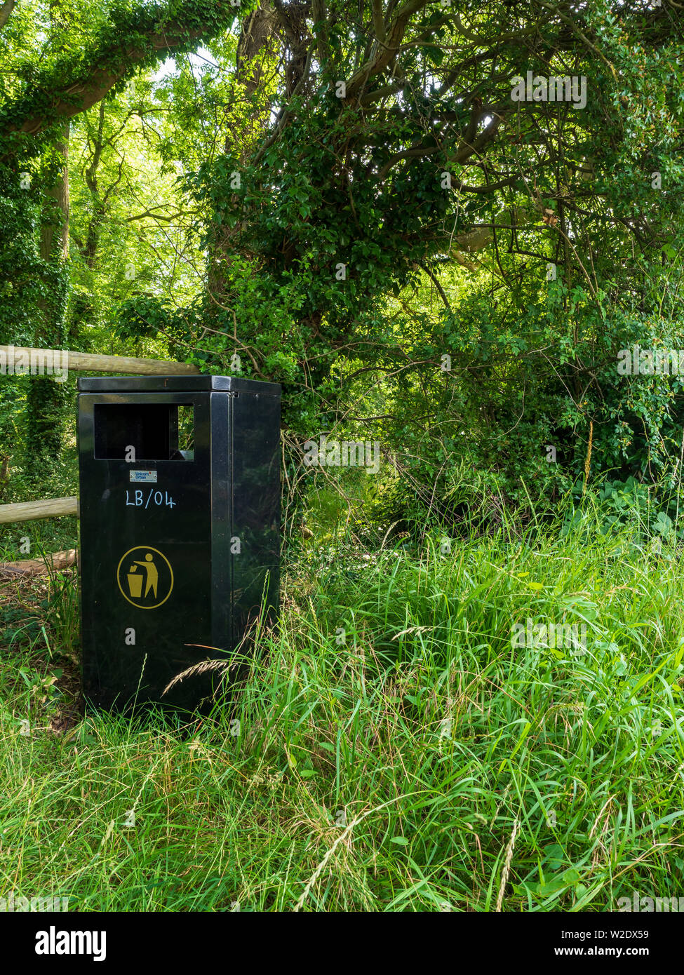 Green metal dustbin provided by the council next to a public footpath in woodland to encourage people not to drop litter Stock Photo