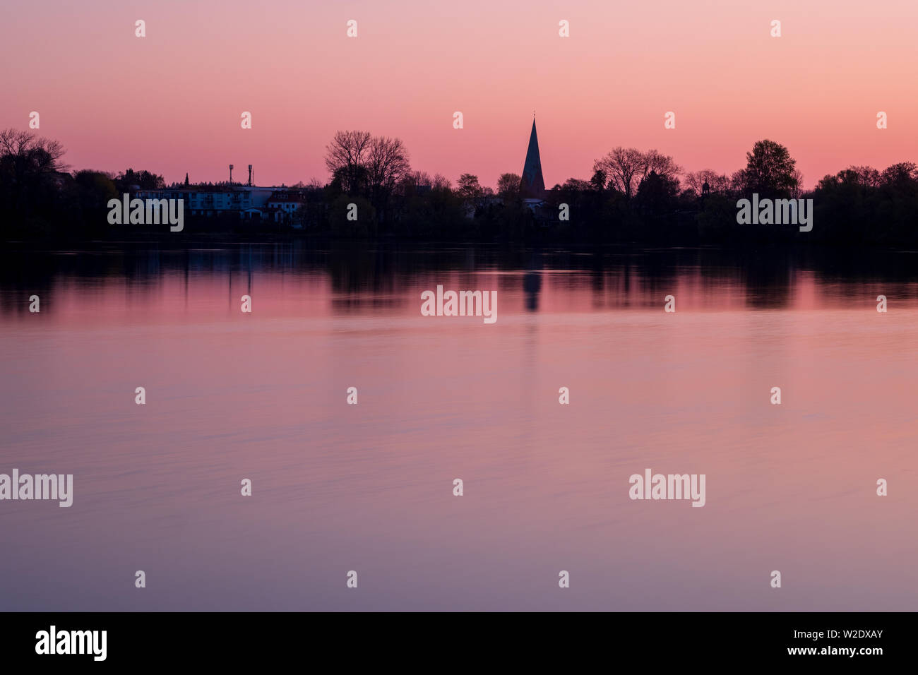 Red and pink sunset over peaceful lake with silhouette of the city of Eutin with churchtower, Schleswig-Holstein Stock Photo