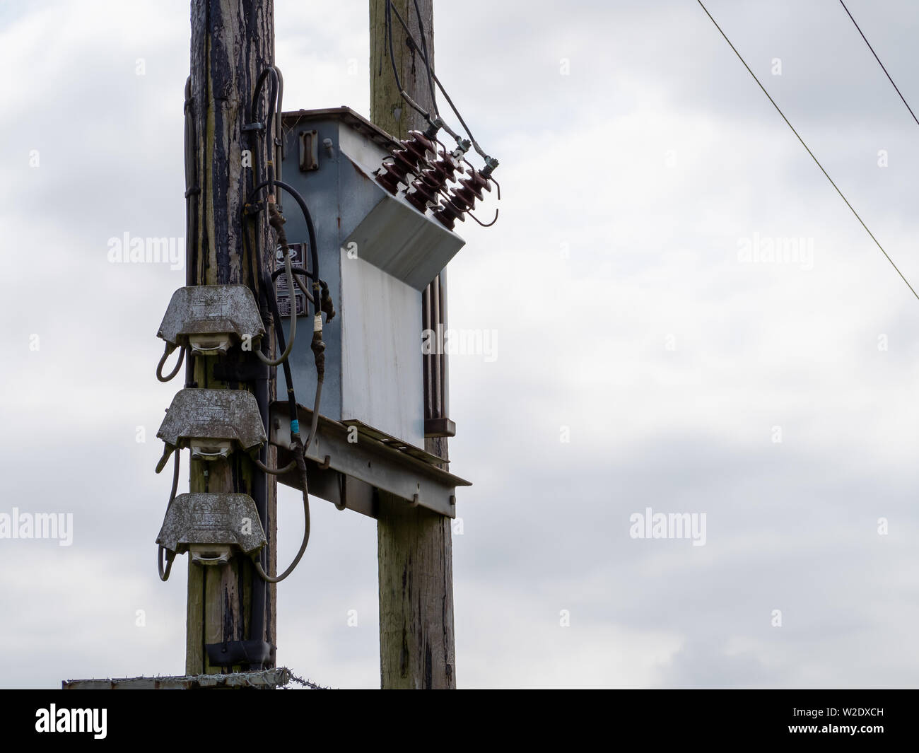 Transformer on twin electric poles with fusible links isolated against the sky Stock Photo