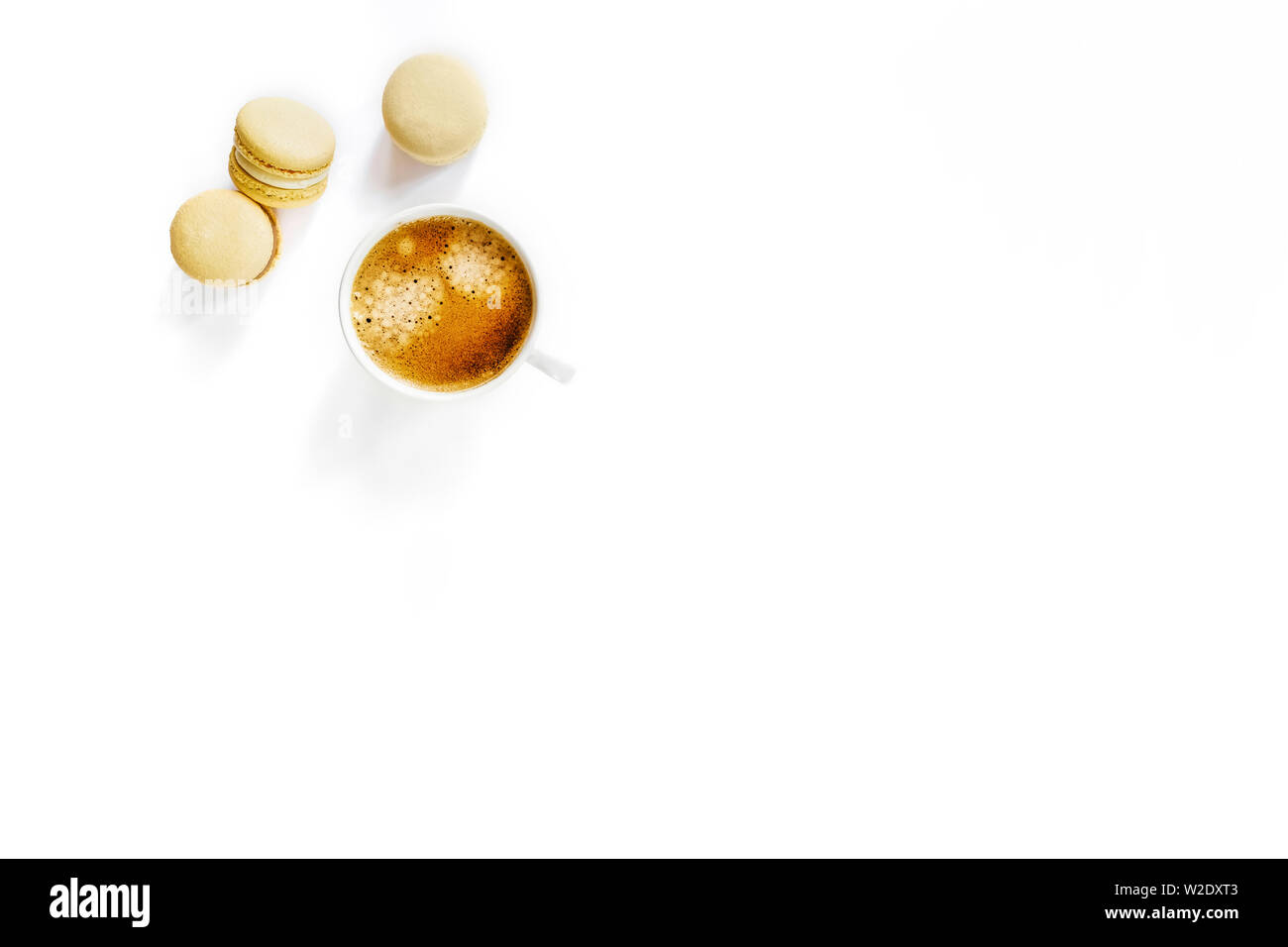 White cup of tasty coffee on white isolated desk with three yellow macarons. Stock Photo