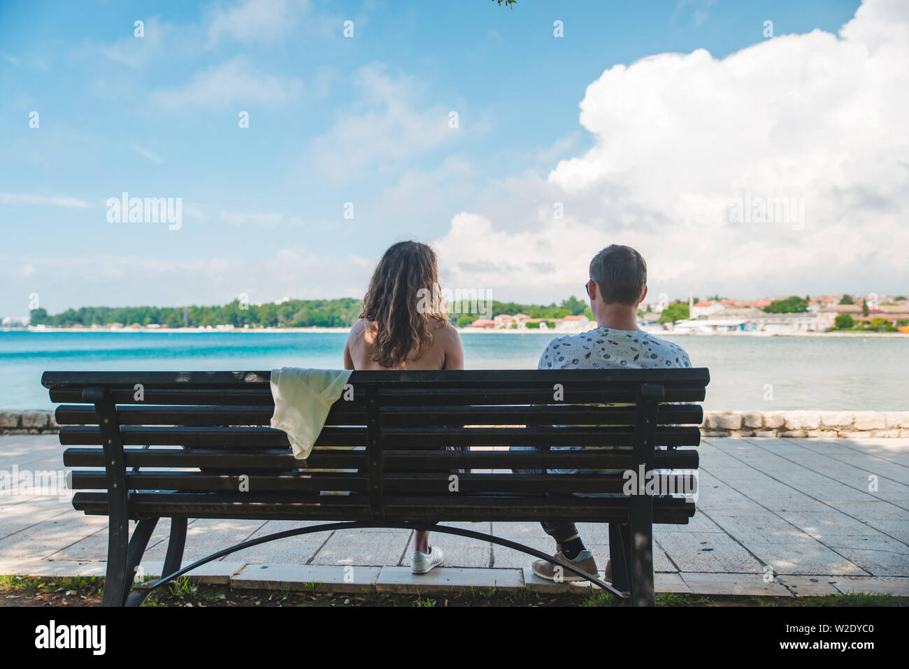 couple travelers sitting on bench with sea view resting in shadow. hot ...