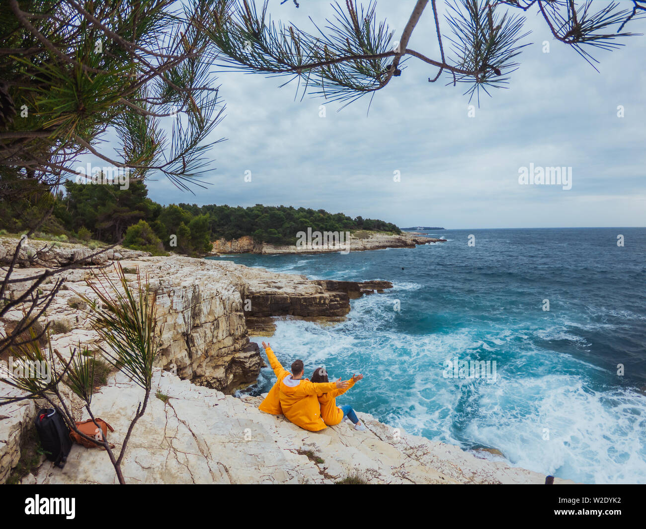 smiling couple in yellow raincoats at the edge of the cliff looking at ...