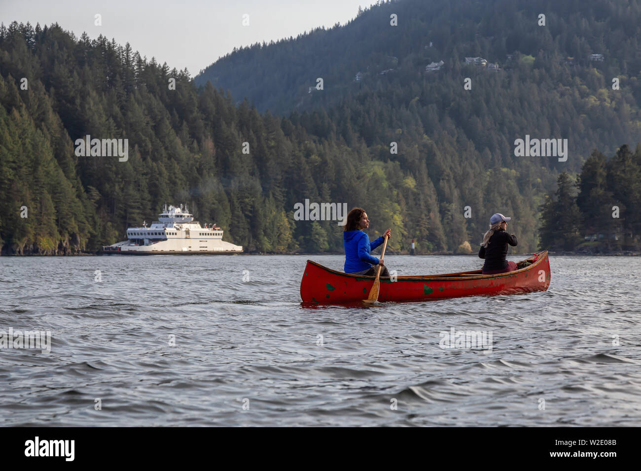 Adventurous friends on a red canoe are paddling in the Howe Sound with