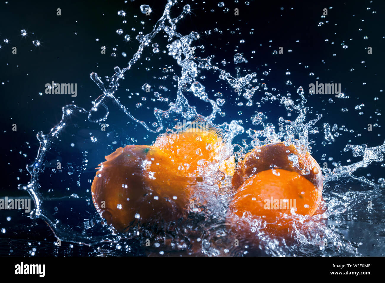 ripe oranges lying on the mirror in a spray of water on dark background Stock Photo