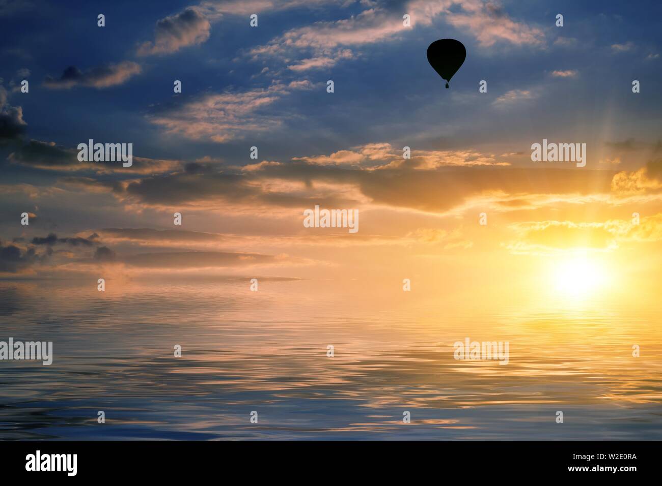 natural landscape with cloudy sky at sunset and air balloon reflected in water Stock Photo