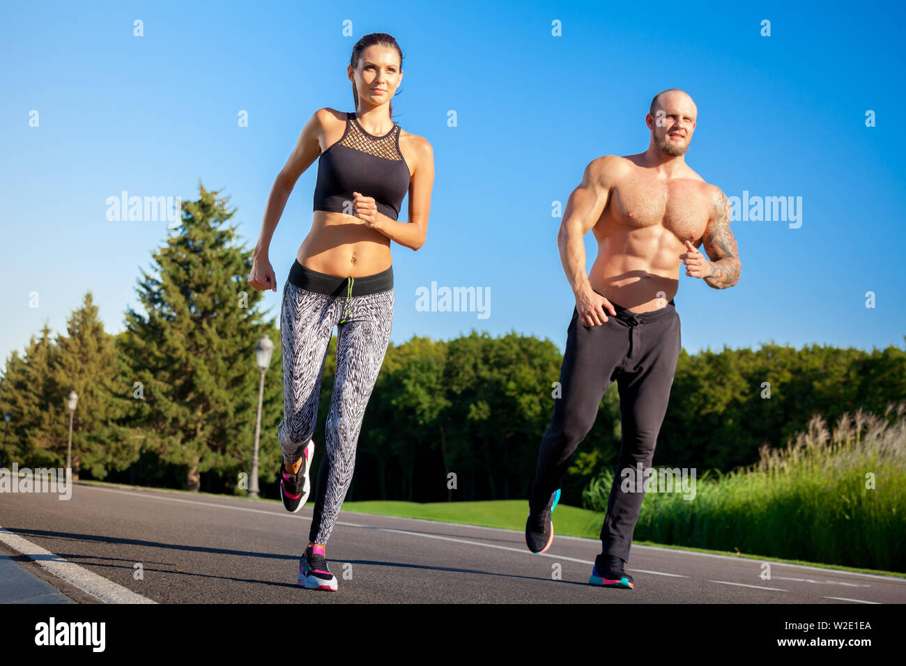 Young strong male and female fitness models outdoors in beautiful landscape. Man and woman running in park Stock Photo