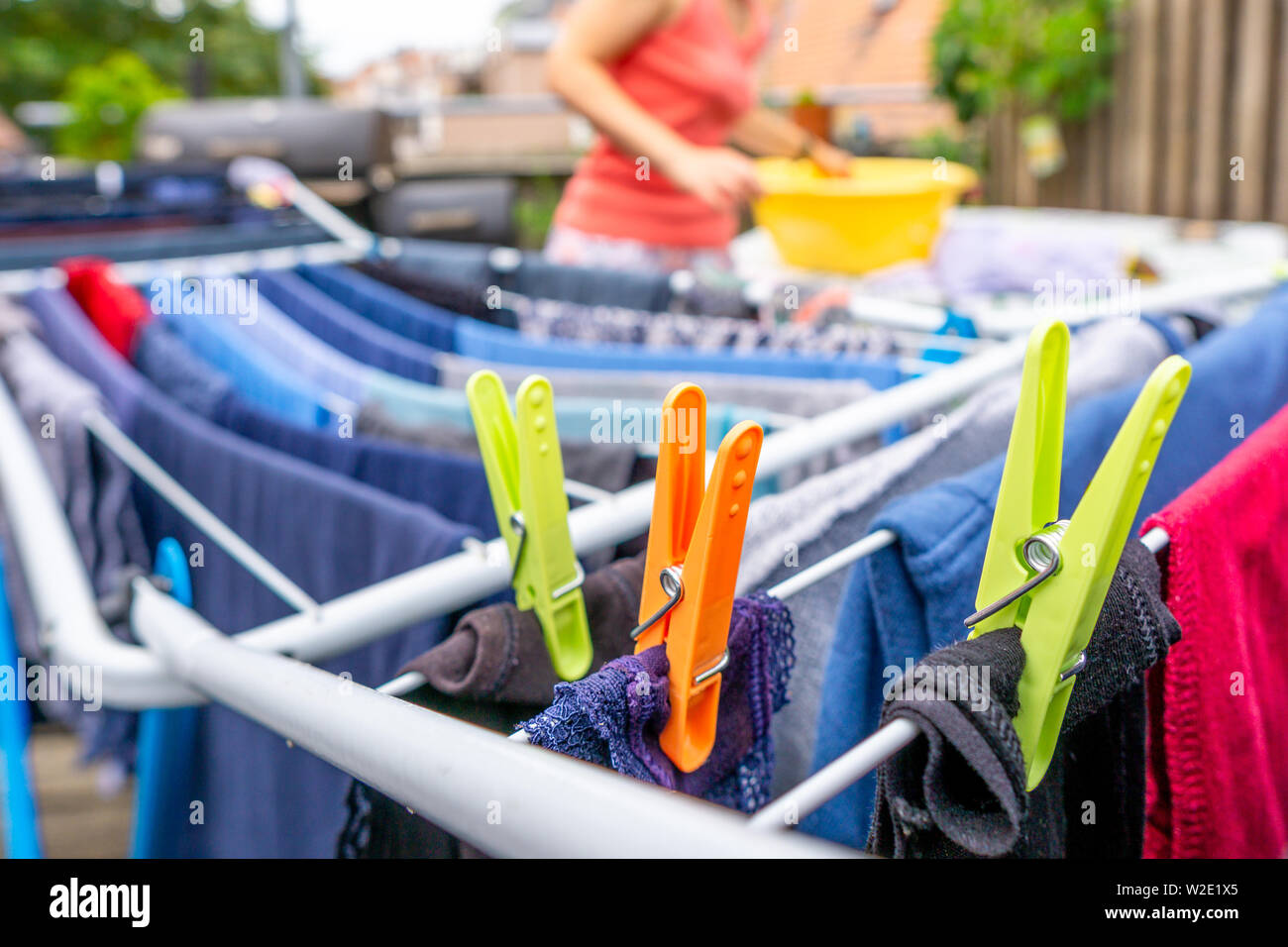 Image of colorful clothespegs on clothline with laundry and blurry woman in the background, cloe up Stock Photo