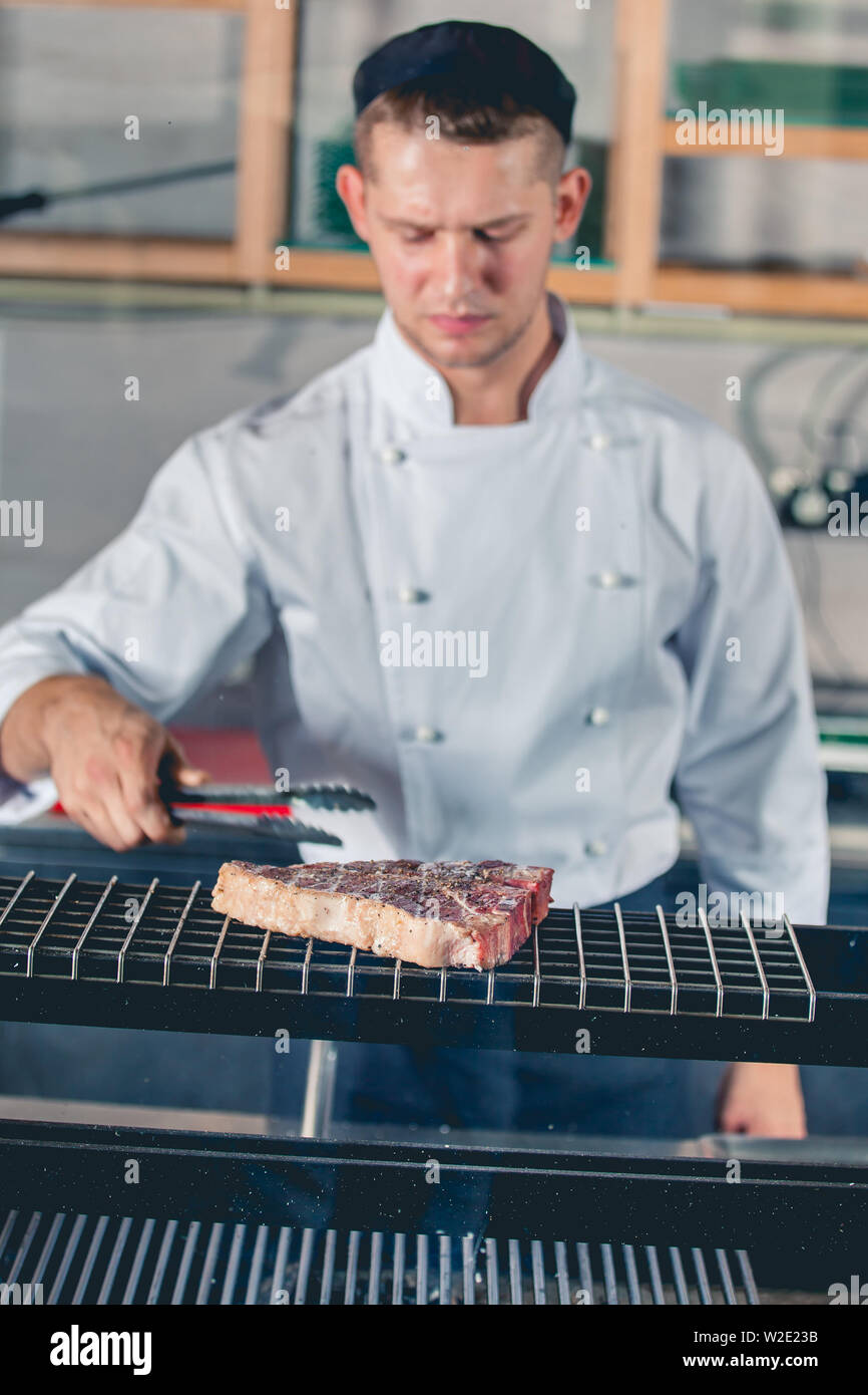 young male cook preparing meal on the grill with metal tongs in hand Stock Photo