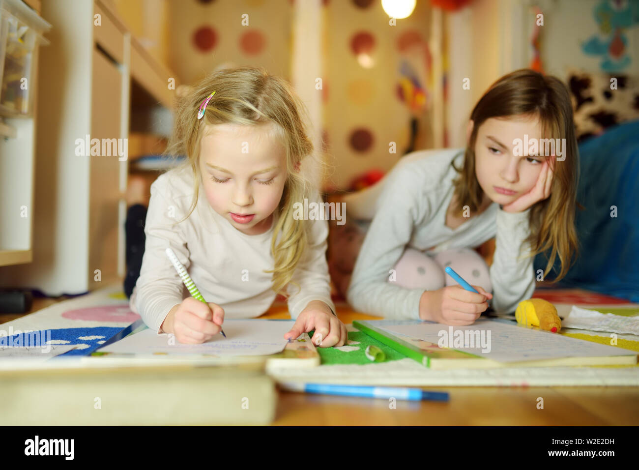 Two cute little sisters writing letters together at home. Older sister