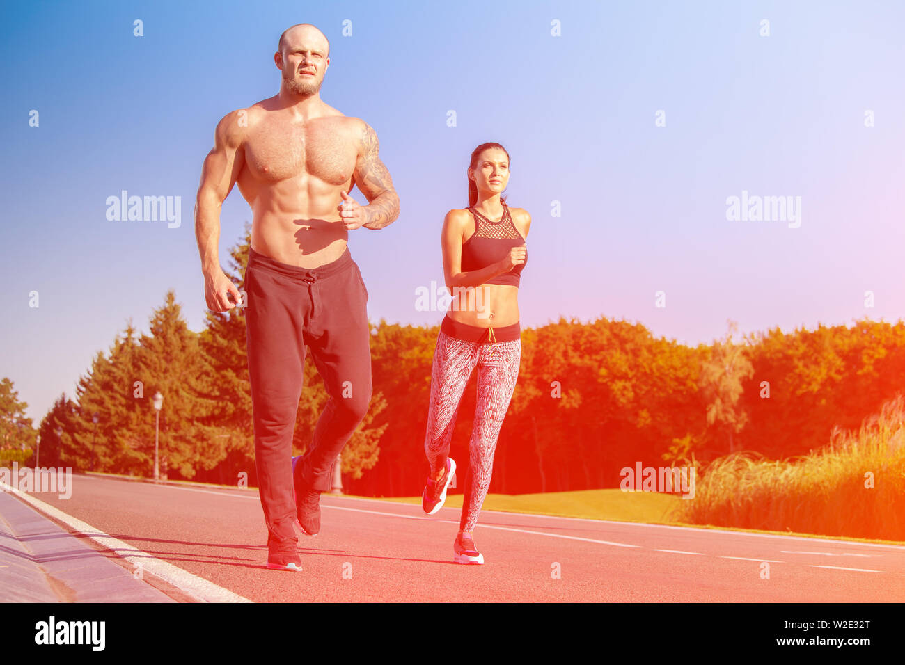 Young strong male and female fitness models outdoors in beautiful landscape. Man and woman running in park at sunset Stock Photo