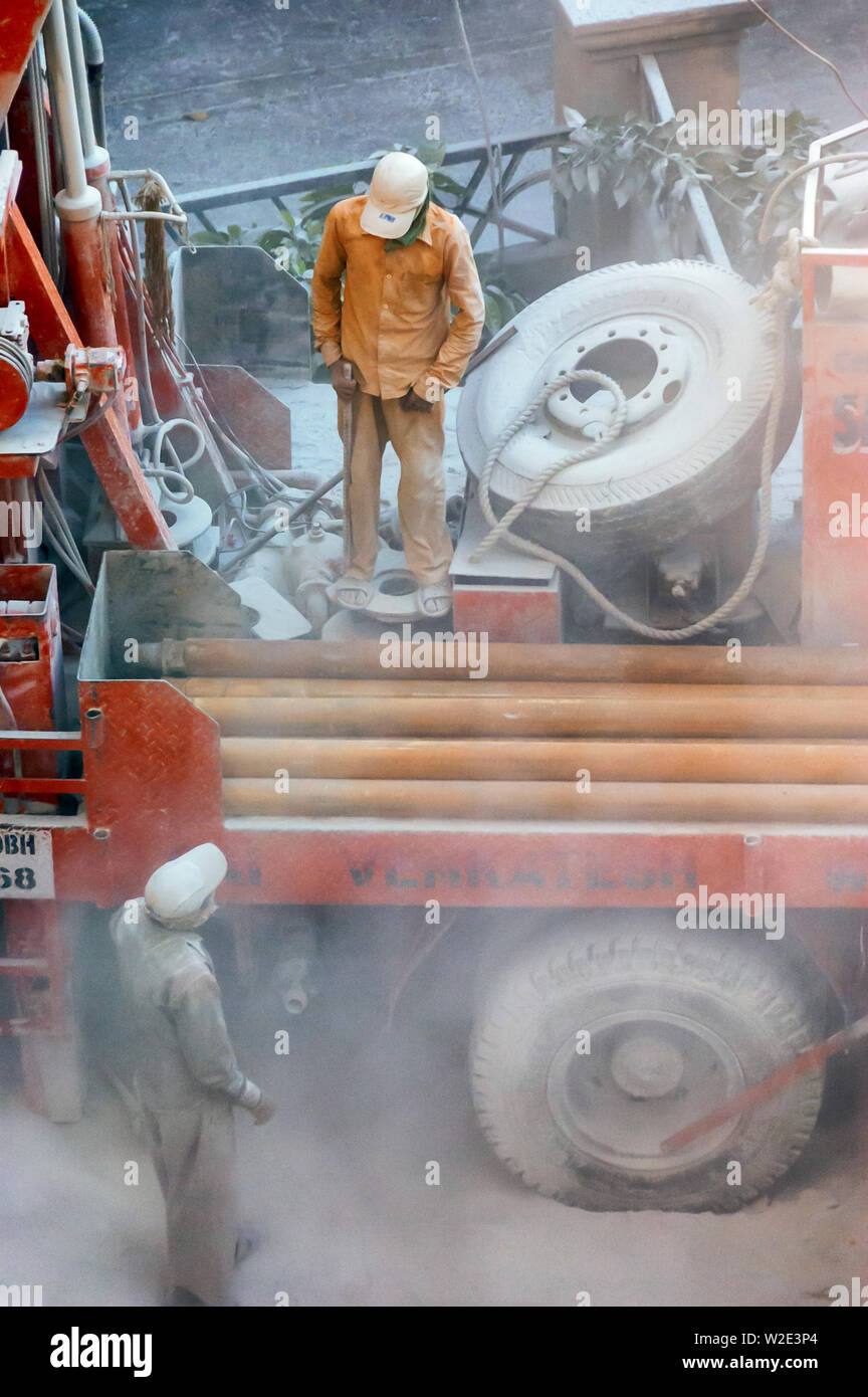 Fine dust floats in the air as two workers of a mobile drilling rig, trying to locate ground water in Hyderabad, India, chats while the machine idles. Stock Photo