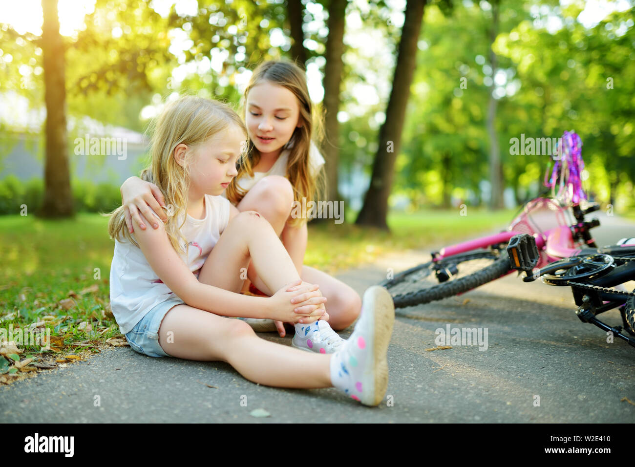 Adorable girl comforting her little sister after she fell off her bike