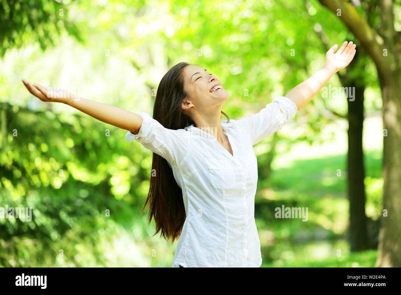 Young woman meditating with open arms standing in fresh spring greenery with her head raised to the sky and her eyes closed rejoicing in the freshness and new beginnings of spring and nature Stock Photo