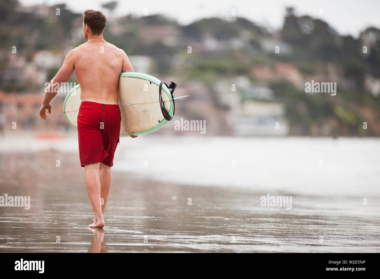 Man walking along the beach with his surfboard Stock Photo - Alamy