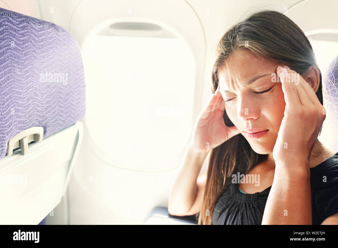 Fear of flying woman in plane airsick with stress headache and motion sickness or airsickness. Person in airplane with aerophobia scared of flying being afraid while sitting in airplane seat. Stock Photo