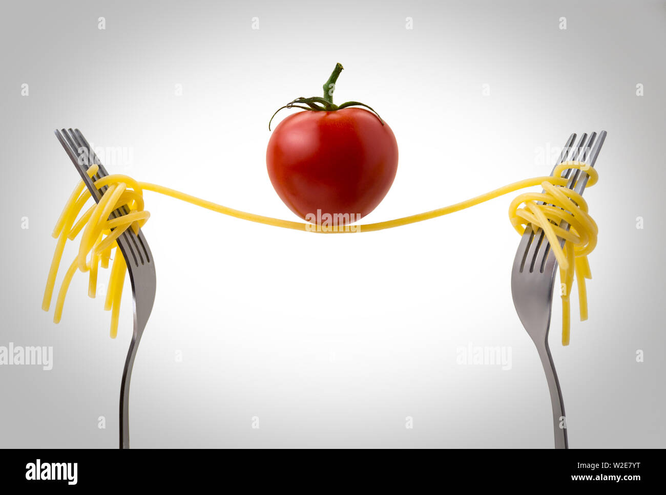 spaghetti between two forks with a tomato above on a white background, abstract photo Stock Photo