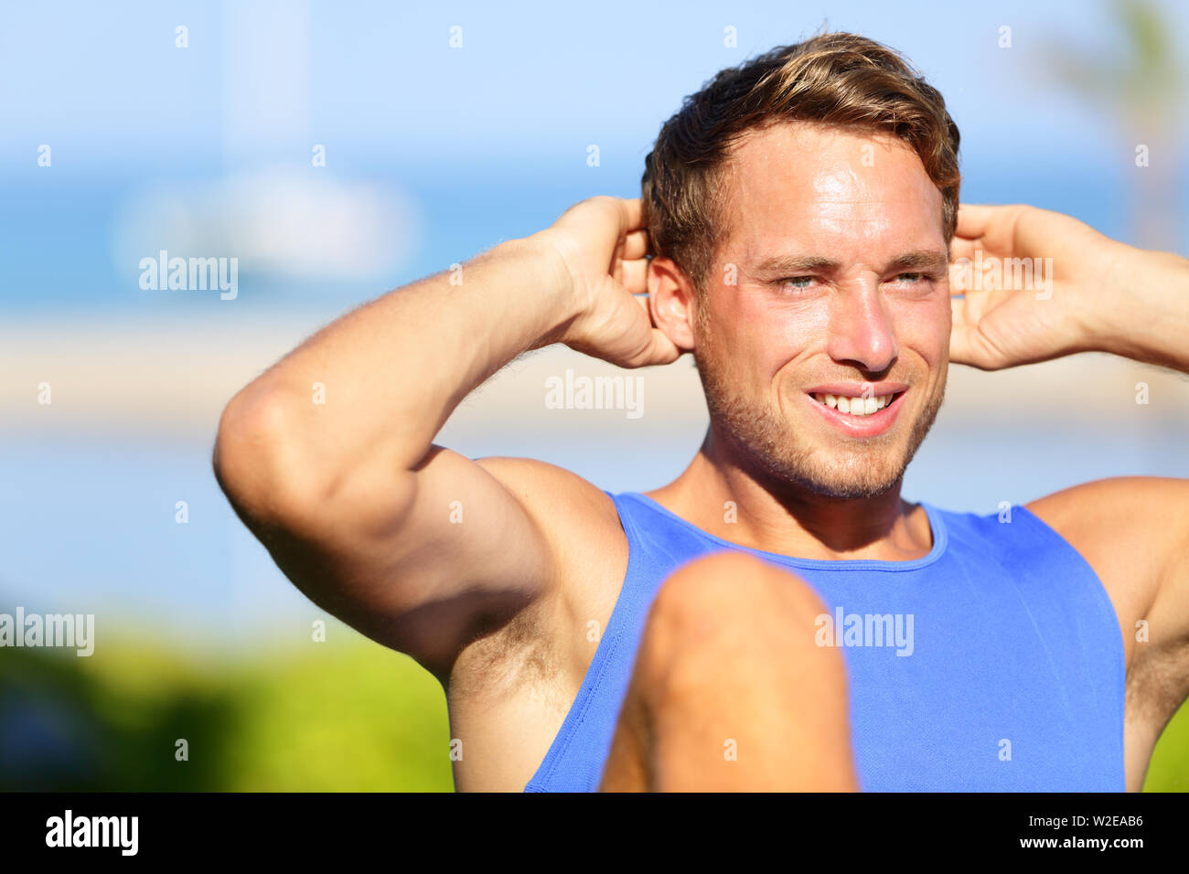 Fitness man doing sit-ups outdoor. Close up portrait of male fitness model training sit up exercise during outside workout in grass in summer. Handsome muscular male sport model working out. Stock Photo