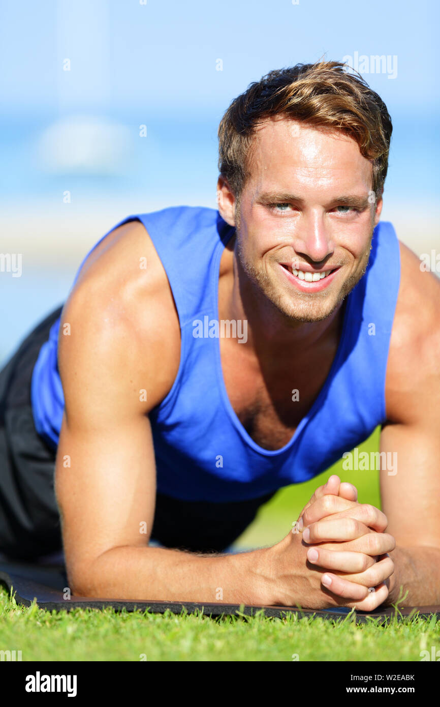 Fitness man training plank core exercise working out his midsection core muscles. Fit male fitness instructor planking exercising outside in summer on grass. Stock Photo