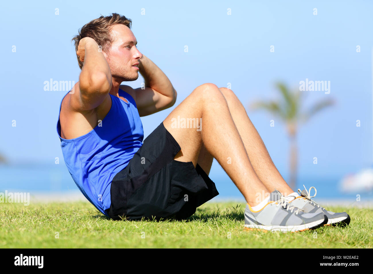 Sit-ups - fitness man training sit up outside in grass in summer. Fit male athlete working out cross training exercising. Caucasian muscular sports model in his 20s. Stock Photo
