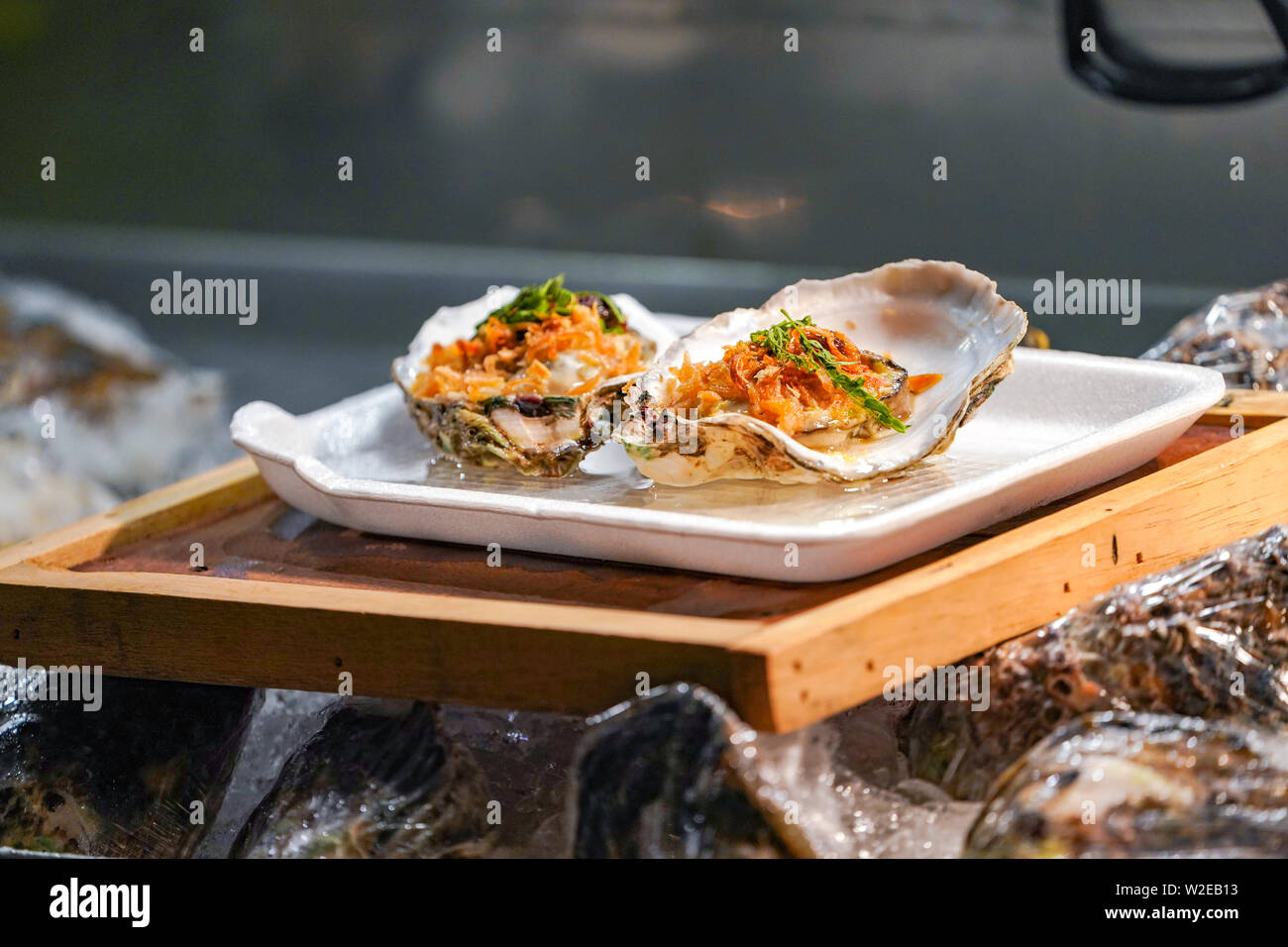 Fresh Raw big couple Oysters on the foam dish and wooden plate topping by fried garlic and leaf the ready to serve. Stock Photo