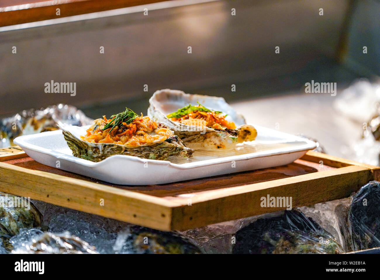 Fresh Raw big couple Oysters on the foam dish and wooden plate topping by fried garlic and leaf the ready to serve. Stock Photo