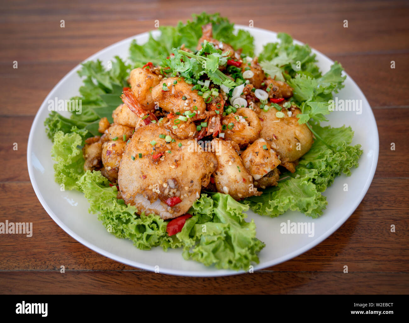 Fried Seafood shrimp prawn fish mussel squid fish on the salad vegetagle in white circle dish on wood table. Stock Photo