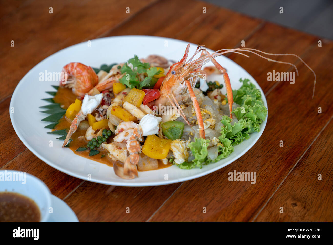 Seafood Thai mixxed together between boiled shrimp, crab, squid and colourful vegetable in dish on wood table in restaurant. Stock Photo